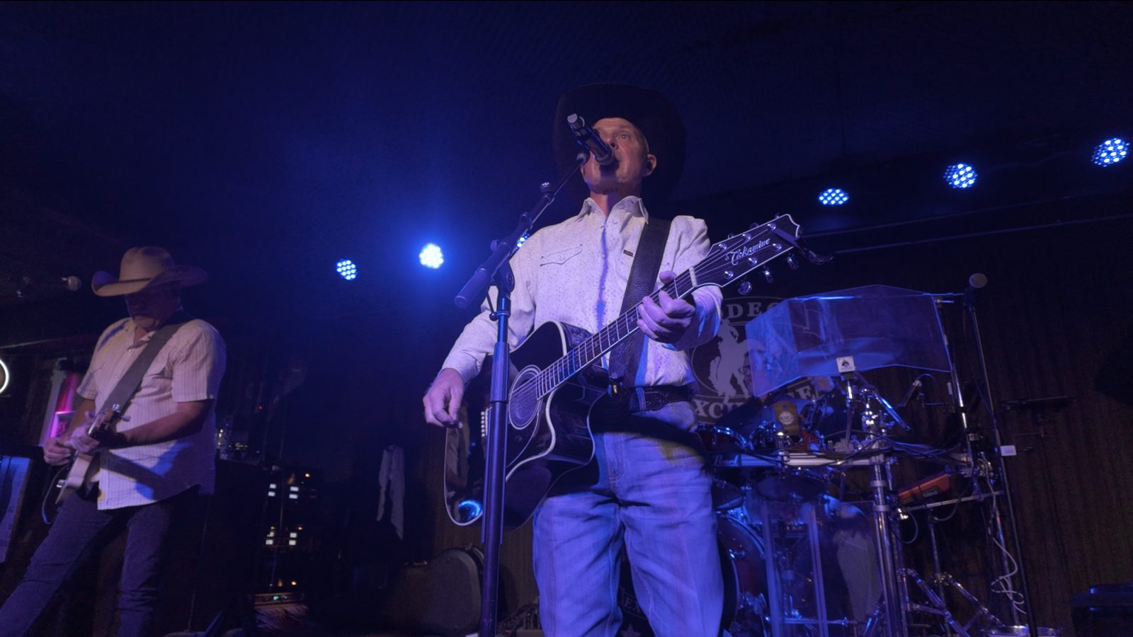 Honkytonk U on stage at Rodeo Exchange, the singer at the microphone with a guitarist behind him.